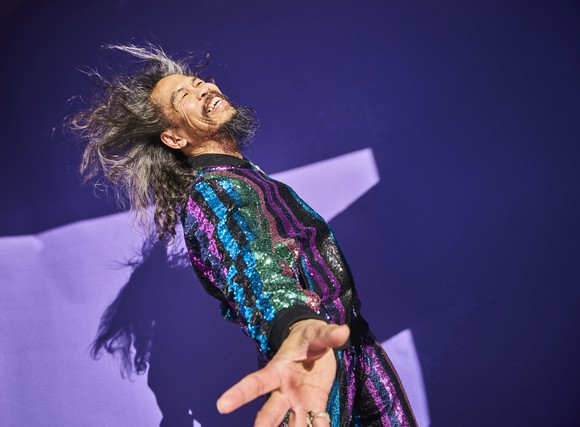 happy person in colorful disco outfit dancing against purple background