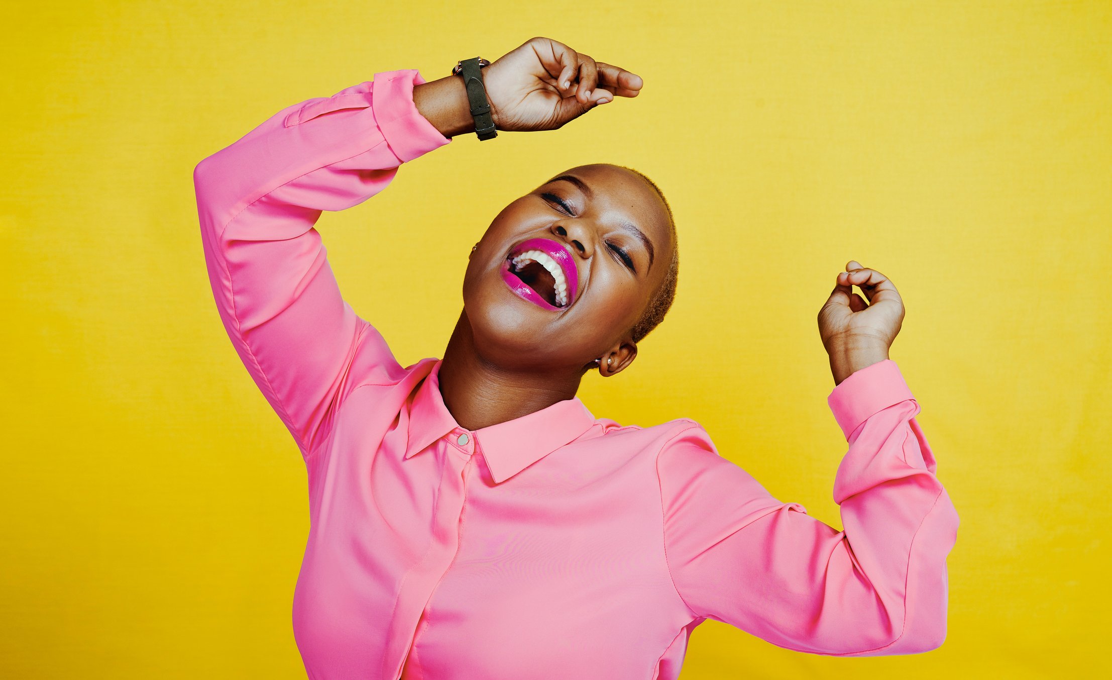 Happy person in bright pink shirt dancing and smiling against yellow background.