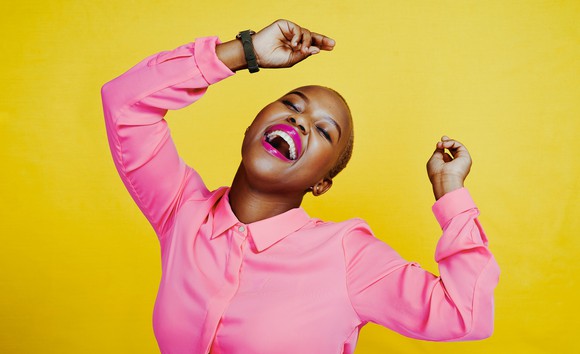 Happy person in bright pink shirt dancing and smiling against yellow background.