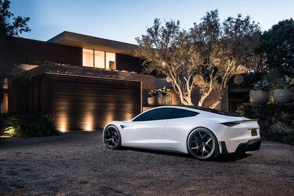 Tesla Roadster parked in front of a house at twilight.