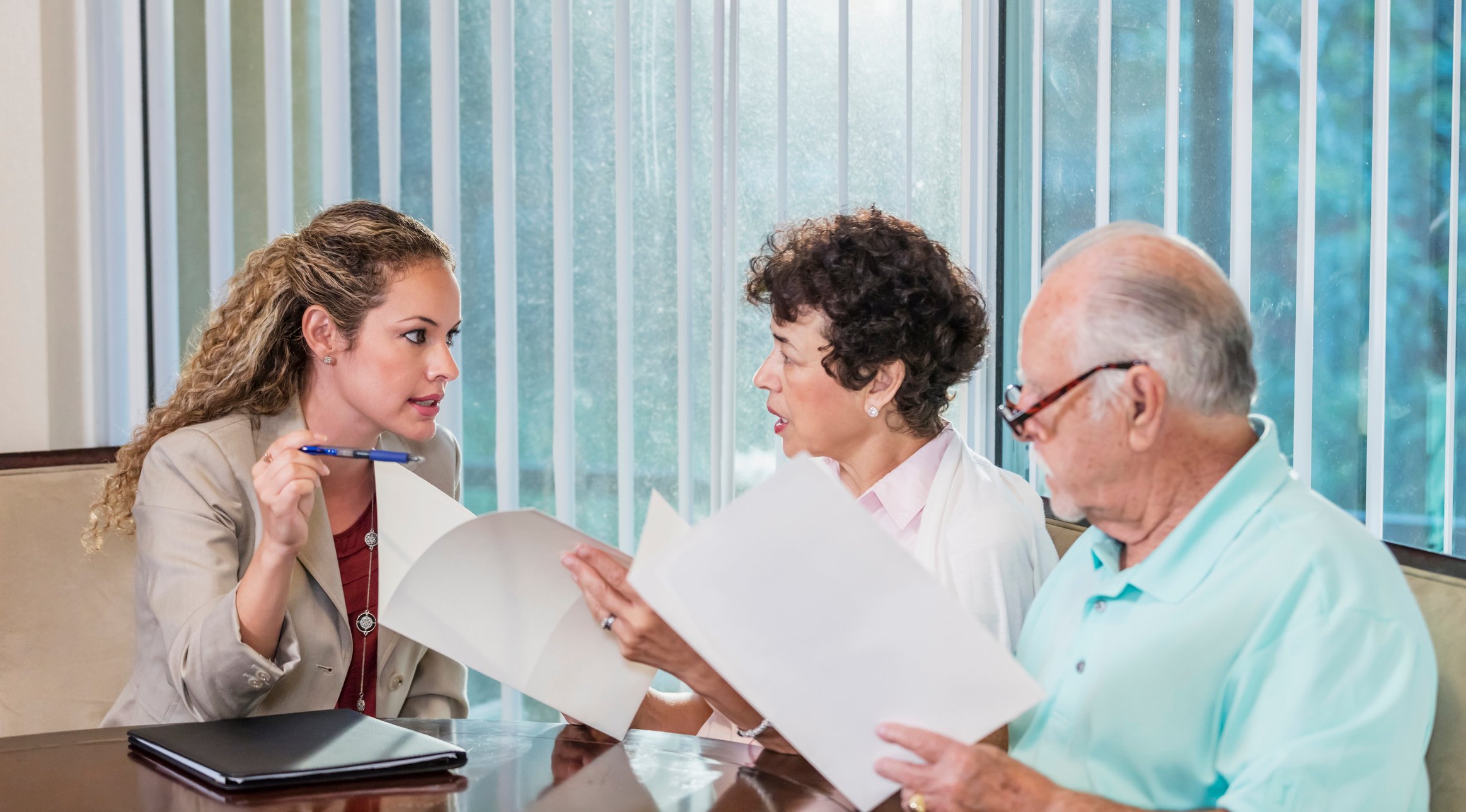 Three people discussing pamphlets of papers at an office table.