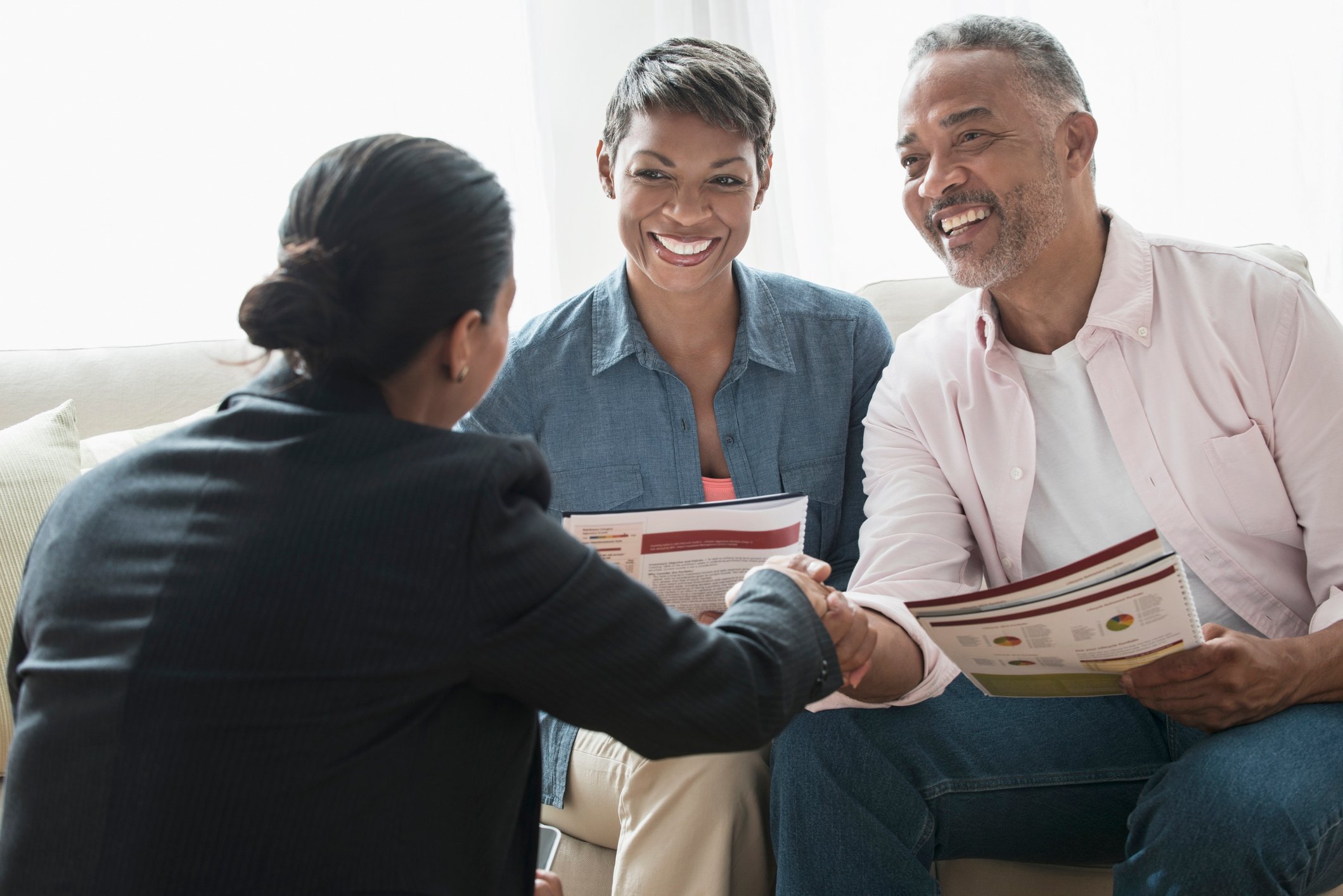 Two people holding documents and shaking hands with a third person.