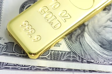 A gold bar rests on a one hundred dollar bill.