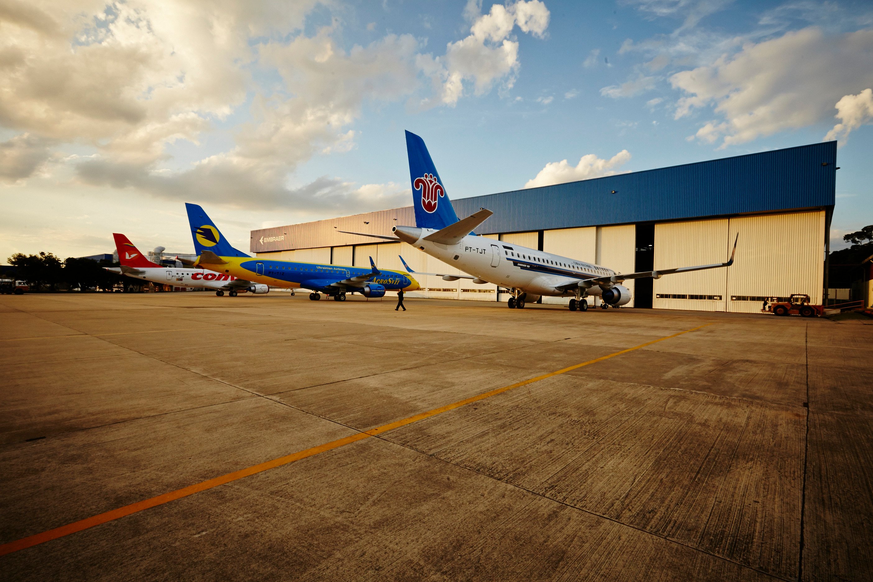 Three Embraer jets parked outside an Embraer hangar. 