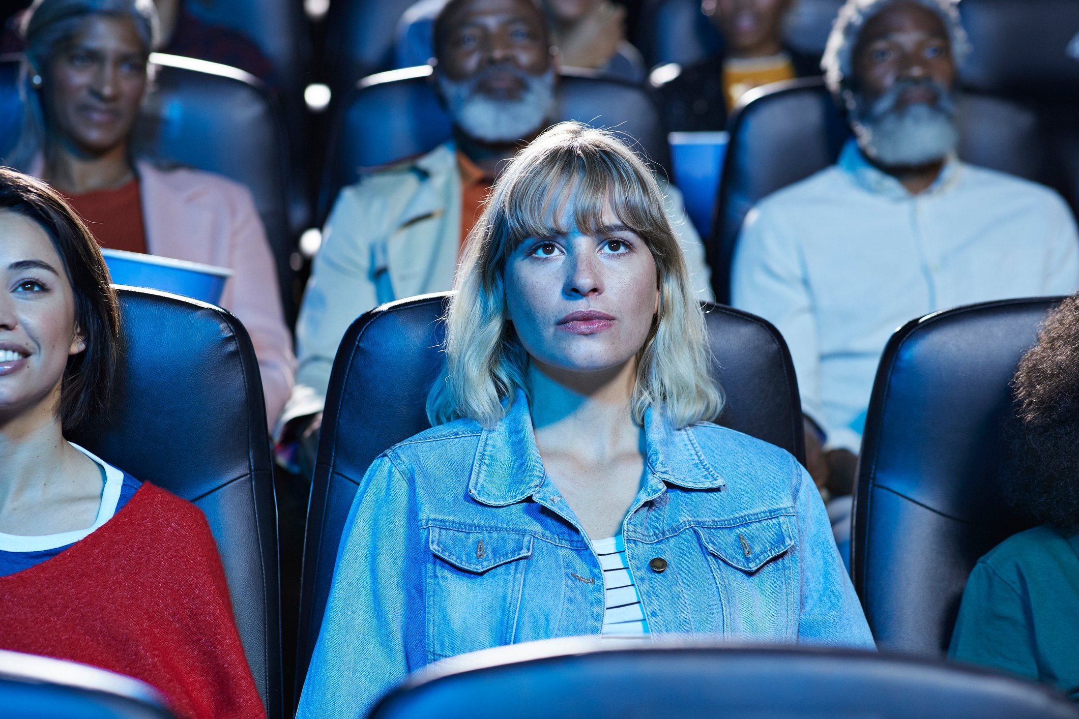 Spectators sitting side by side while watching a movie in a theater. 