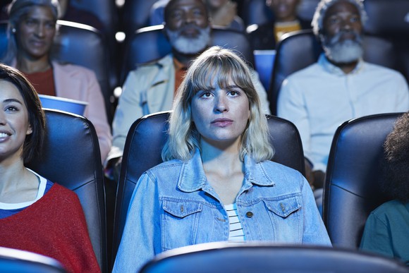 Spectators sitting side by side while watching a movie in a theater. 
