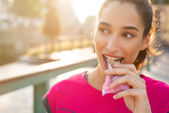 A woman eating a snack bar outdoors.