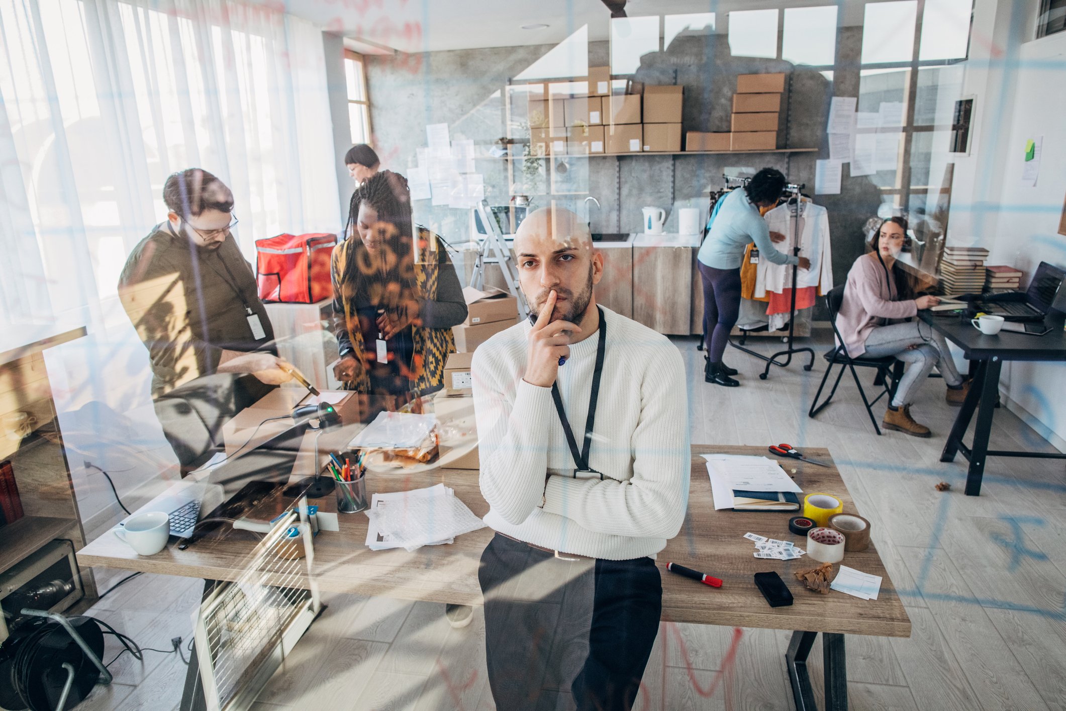 A merchant stands in a co-working space looking off in thought.