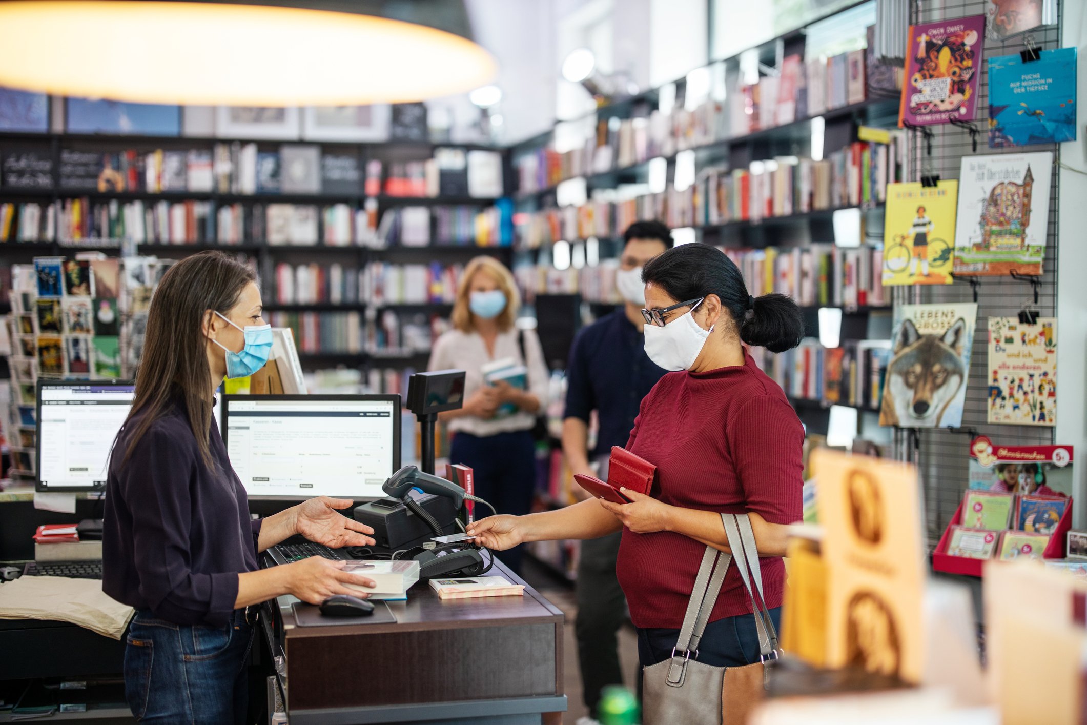 A customer making a purchase in a bookstore where everyone is wearing a COVID mask.