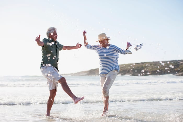 A senior couple playfully kicking water while vacationing on a beach.