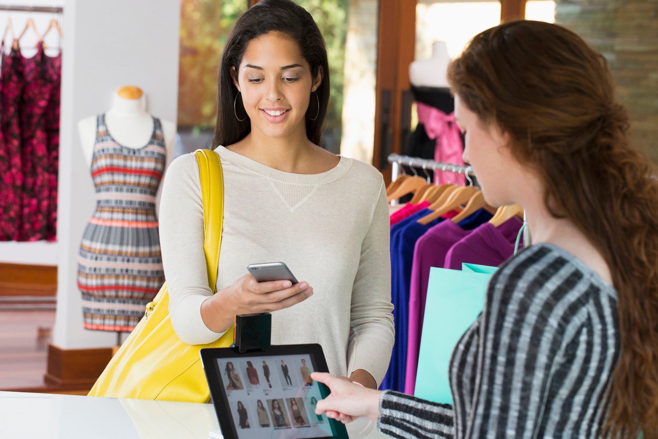 A customer and a salesperson interact with devices at a clothing store.