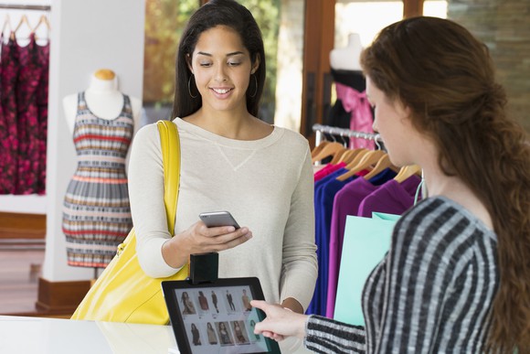 A customer and a salesperson interact with devices at a clothing store.