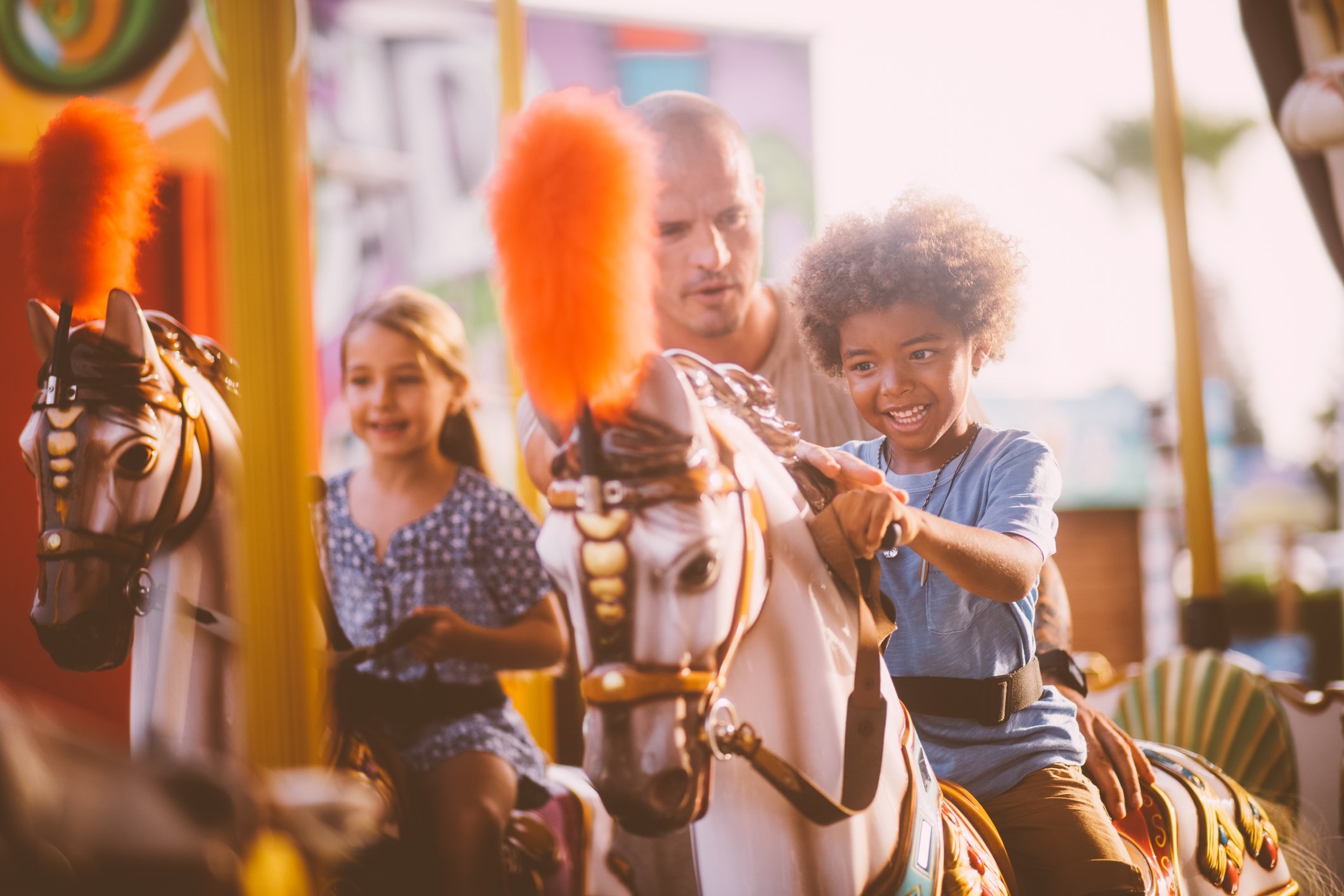An adult standing between two children riding horses on a merry-go-round.