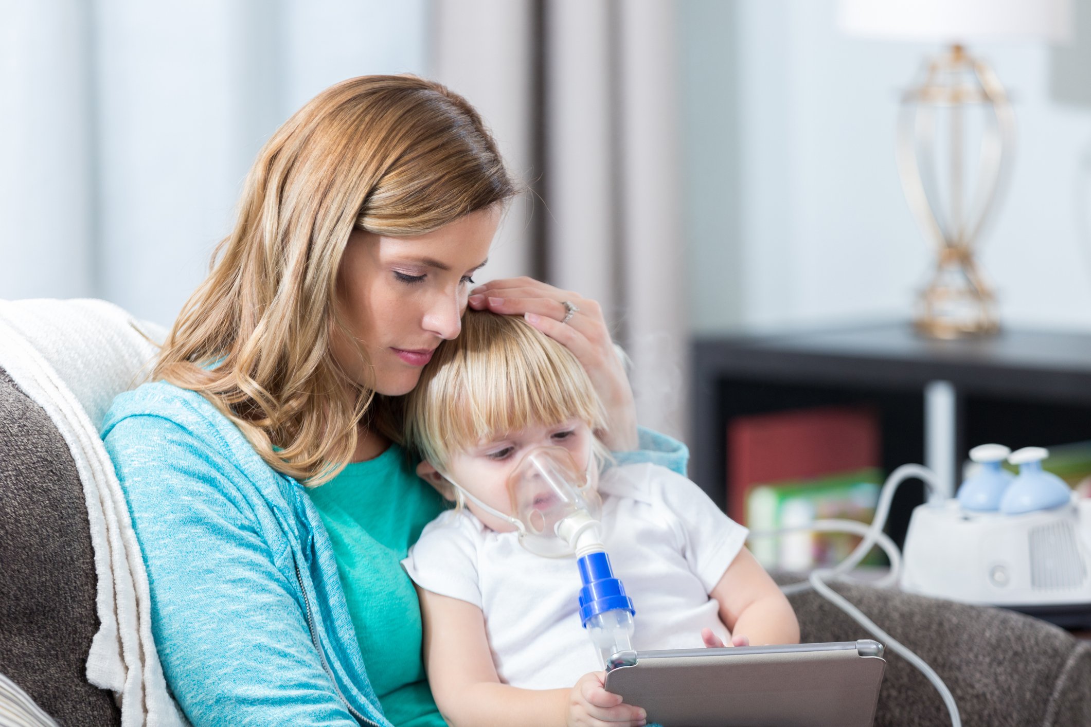 Adult holding a small child receiving a breathing treatment.