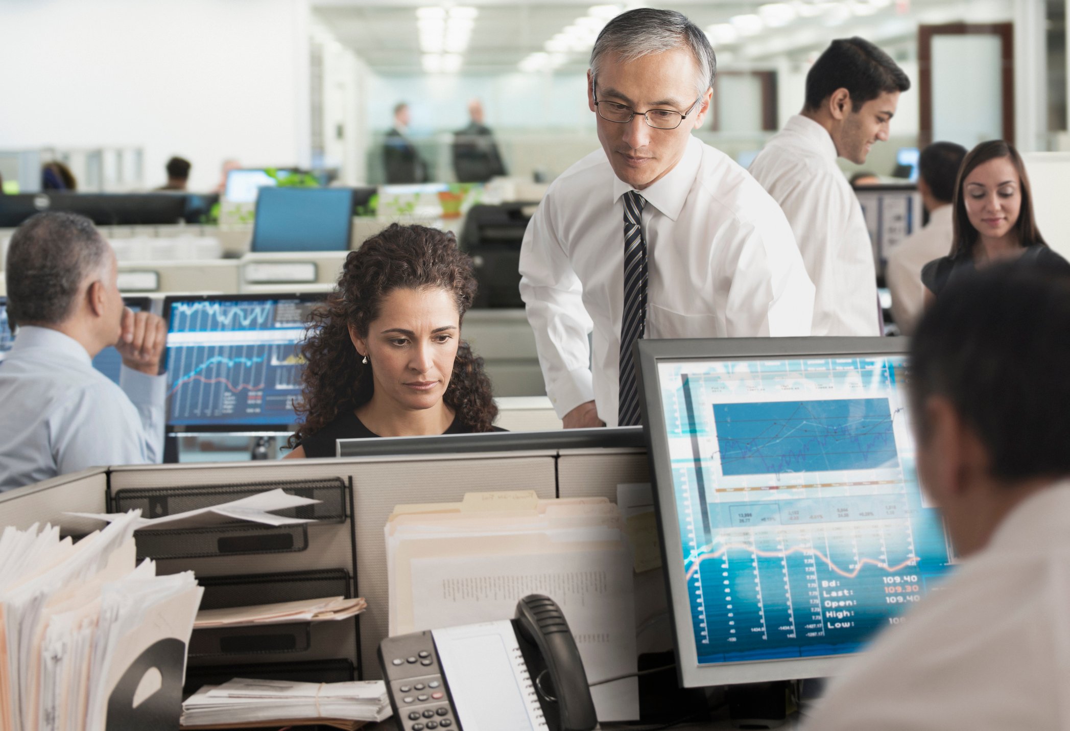 An open office with people at their computers looking at financial data on monitors.
