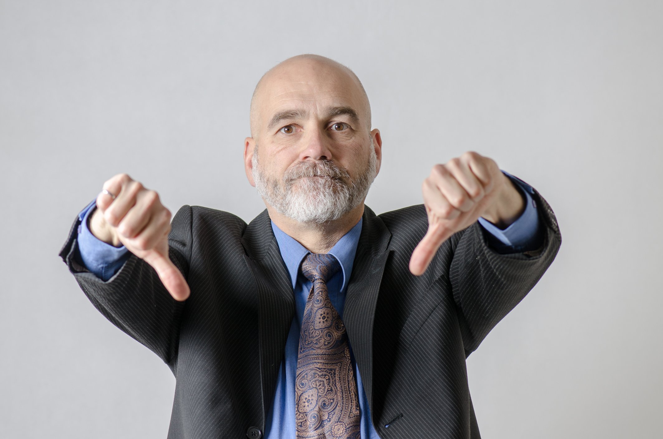 Businessperson in suit and tie showing two thumbs down.