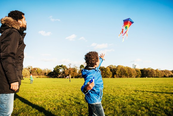 An adult and child fly a kite together on a sunny day. 