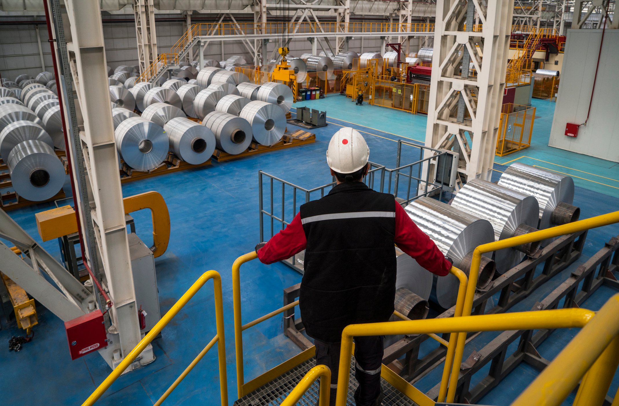 Worker wearing hard hat viewing factory floor with rolls of aluminum.