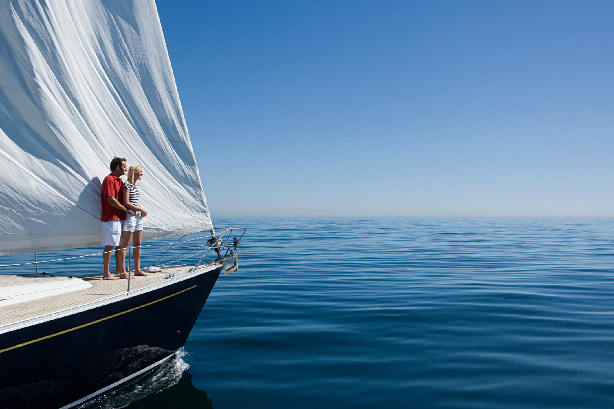 Couple standing on deck of beautiful yacht sailing on crystal blue waters.