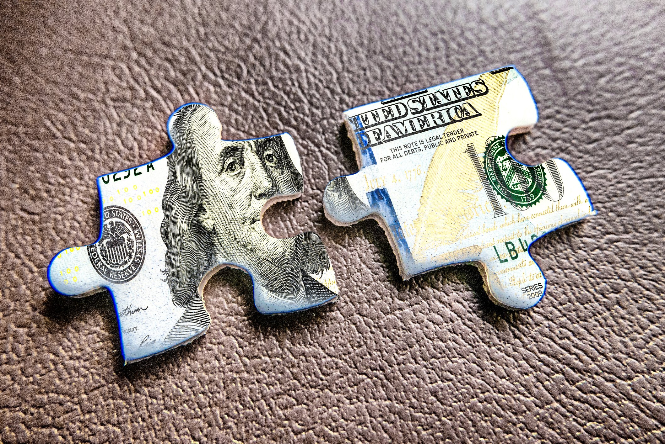 Two jigsaw puzzle pieces showing part of a $100 bill.