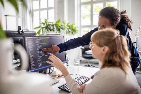 two women point to a computer screen to discuss what they see on the screen