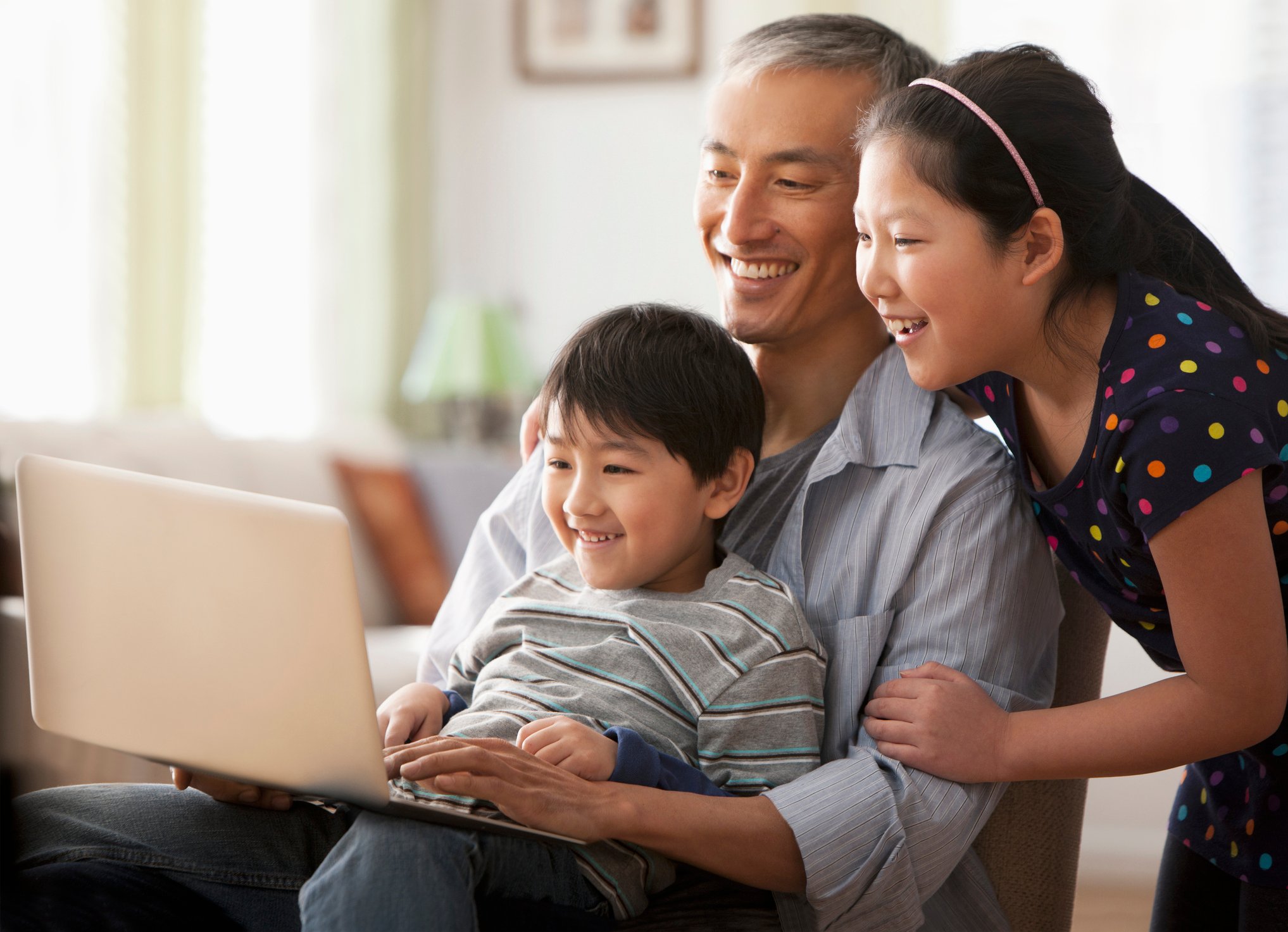 A smiling adult with two smiling children looking at a laptop.