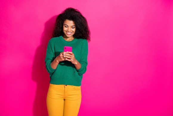 Woman engaging with mobile phone against a Lemonade-pink background.