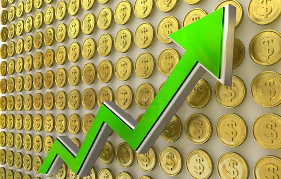 A green uptrend arrow against a background of gold coins bearing the dollar sign. 