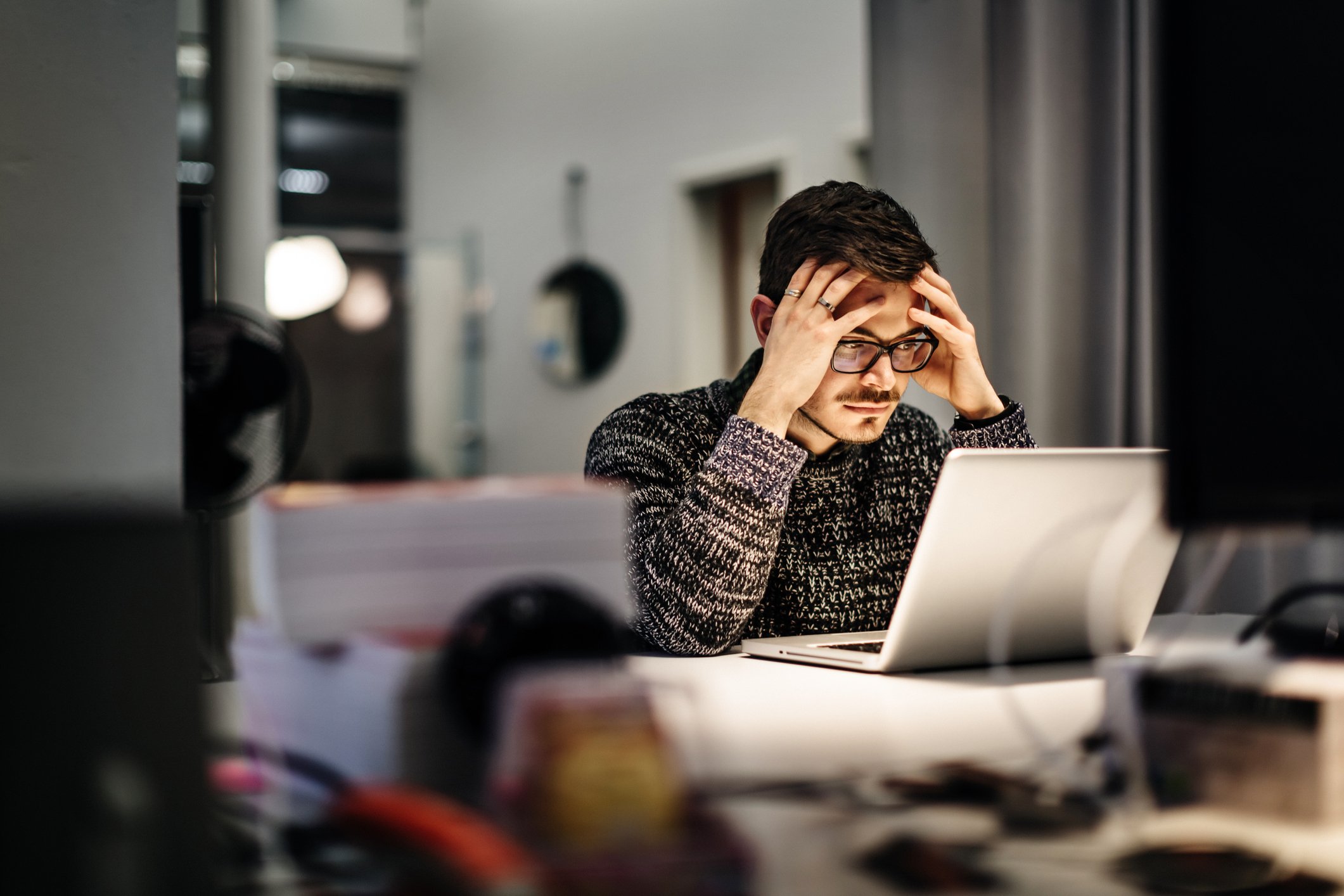 A person holding their head while looking at a laptop.