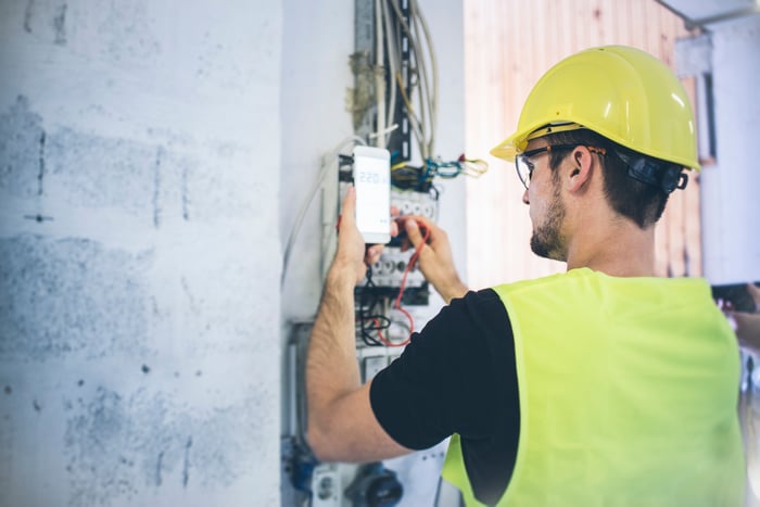 Telecom technician works on equipment while holding a smartphone.