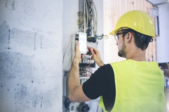 Telecom technician works on equipment while holding a smartphone.