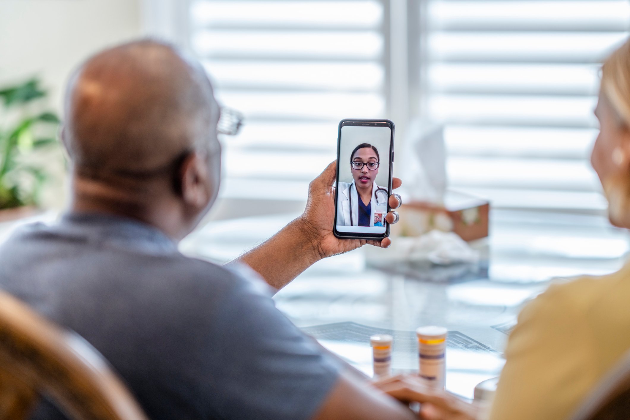 Two people look at a smartphone while consulting with a doctor via video chat.