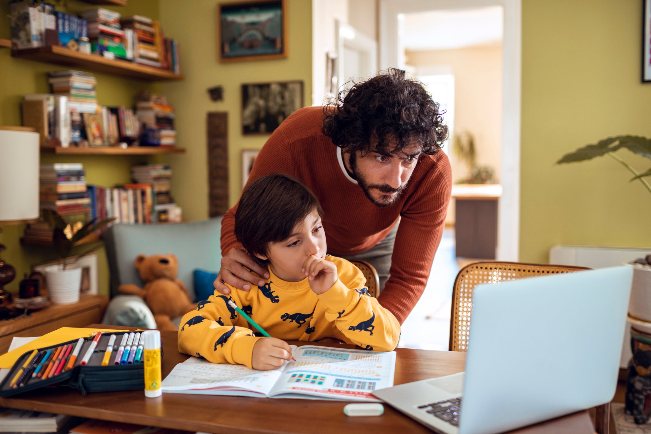 Child doing homework in front of computer as his father leans over him to help.