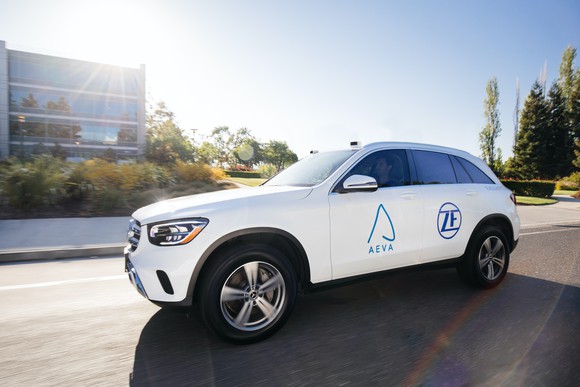 A white Mercedes-Benz SUV with visible lidar sensors and Aeva and ZF logos on its doors. 