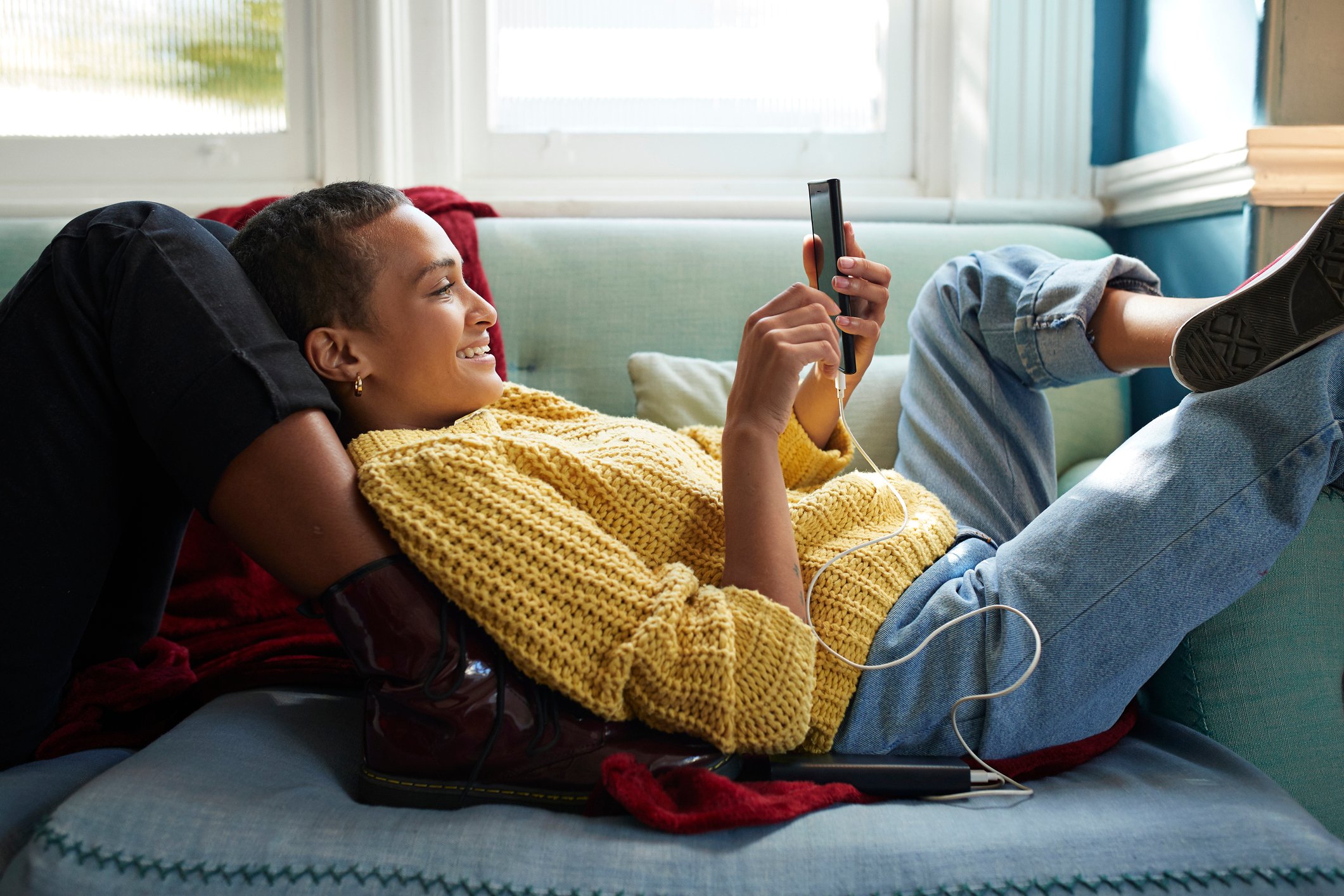 A young person laying on a sofa and wearing jeans.