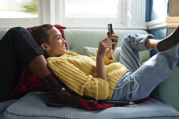 A young person laying on a sofa and wearing jeans.