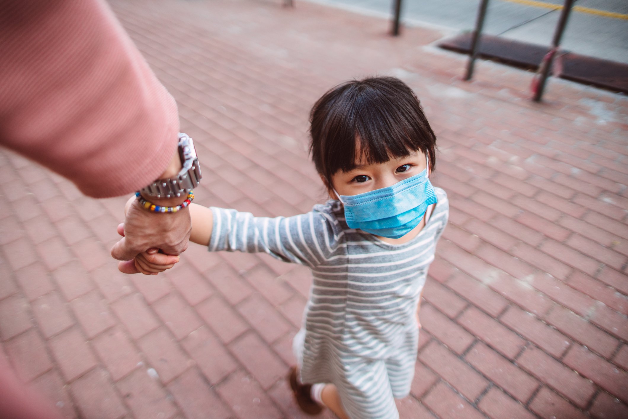 Child in face mask being led by the hand by an adult.