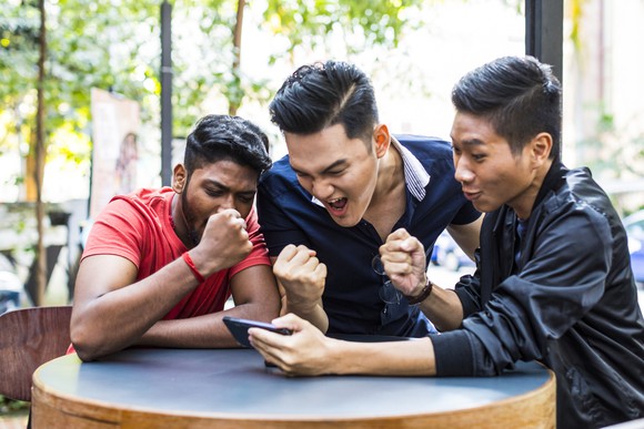 Three men celebrating while looking at a phone.