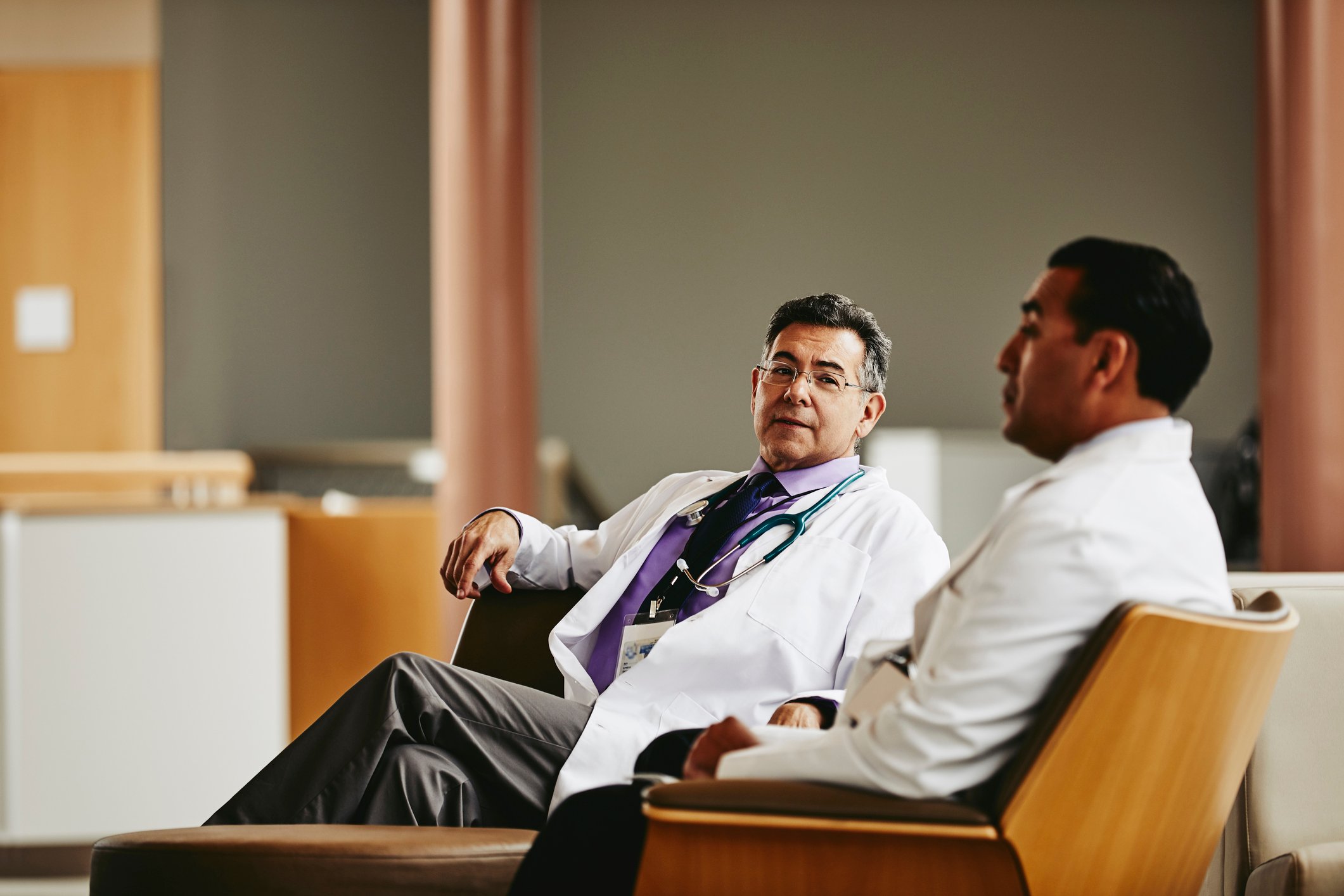 Two doctors chat while sitting in a hospital waiting room.