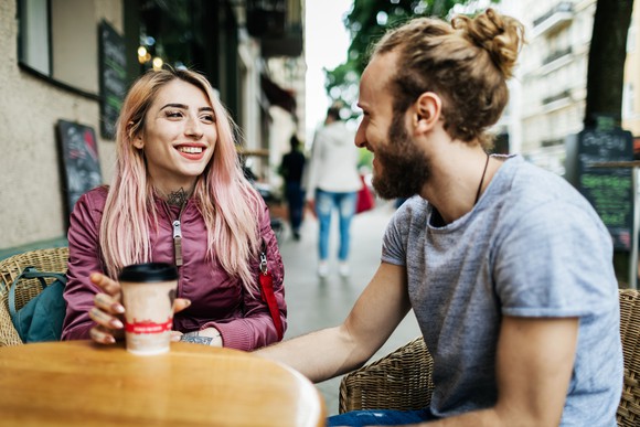 Two smiling people sitting at a table outside having coffee.