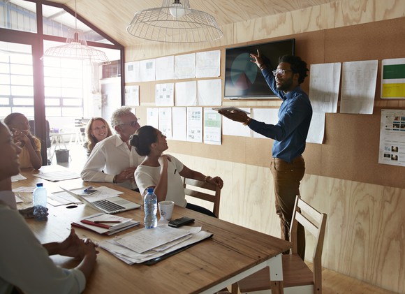 A person presenting to others sitting at a table.