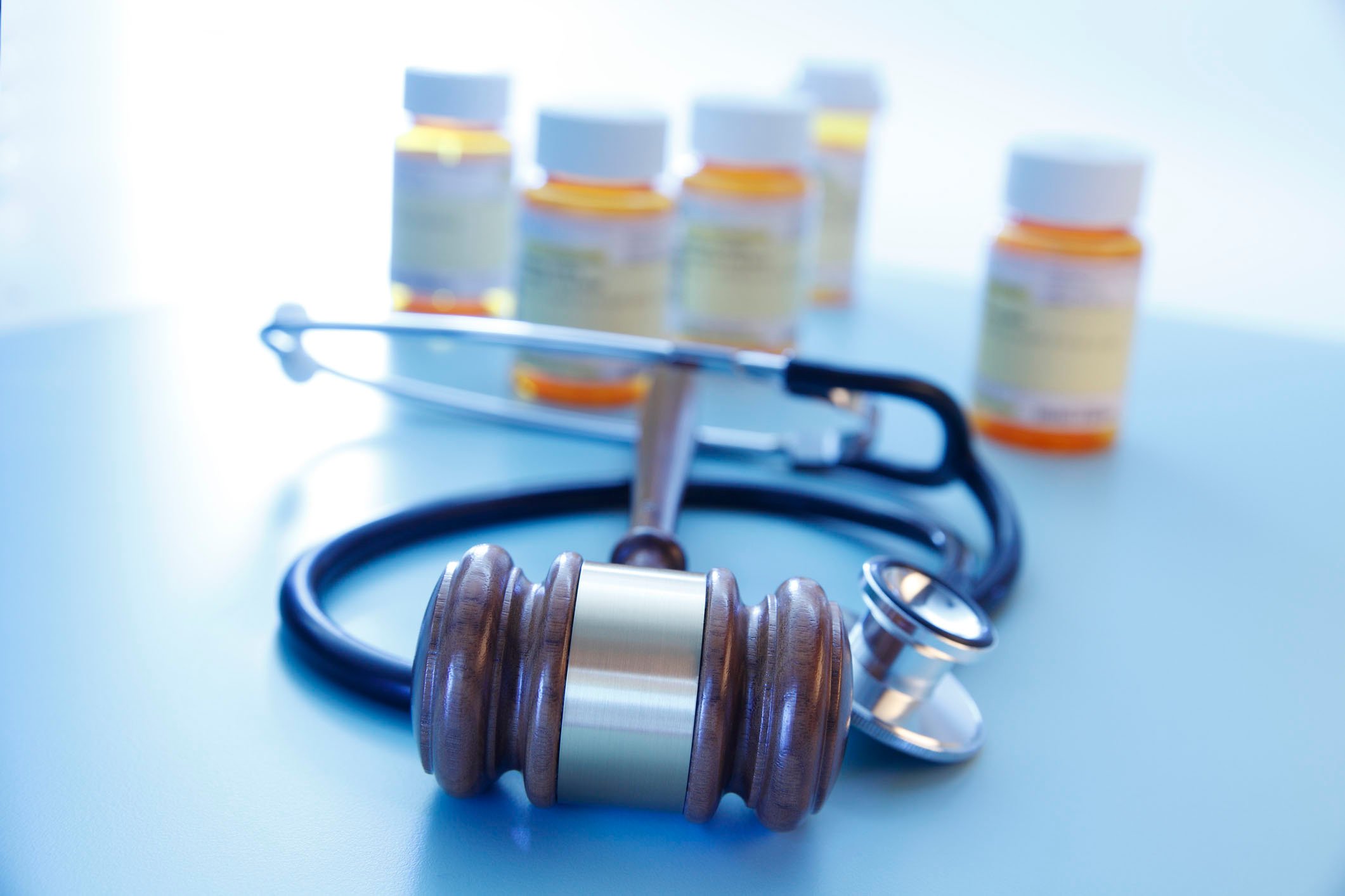 Pill bottles in the background with a court gavel and a doctor's stethoscope in the foreground.
