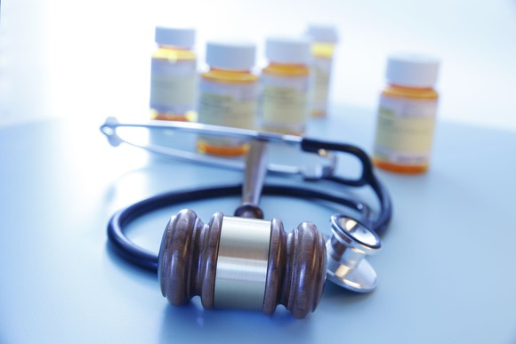Pill bottles in the background with a court gavel and a doctor's stethoscope in the foreground.
