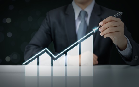 A person is pointing to a stock chart that rises, then falls, then rises again. 