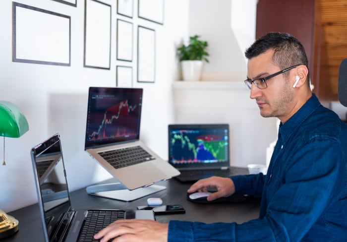 A person sitting at a desk analyzing cryptocurrency movements on three laptops.