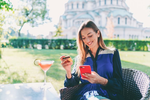 A smartphone user enters credit card information into an app while sipping a cocktail.