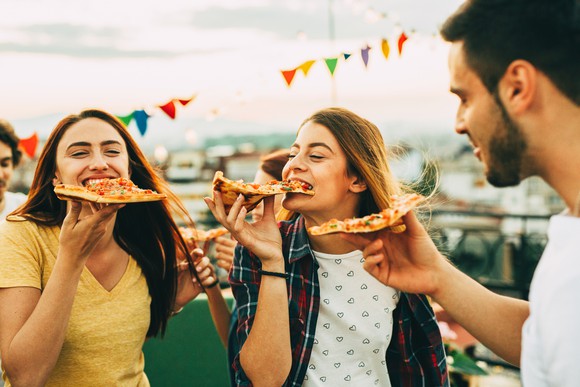 Three people eating pizza on a rooftop.