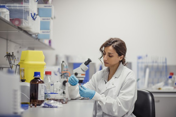 A scientist works at a laboratory bench that's cluttered with bottles and equipment.