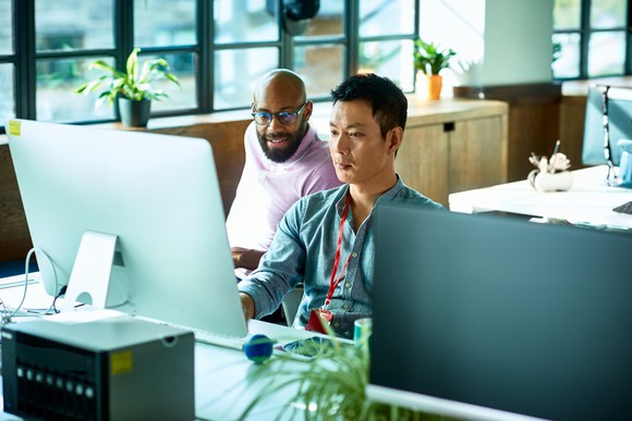 Two people sitting at a desk looking at a computer.