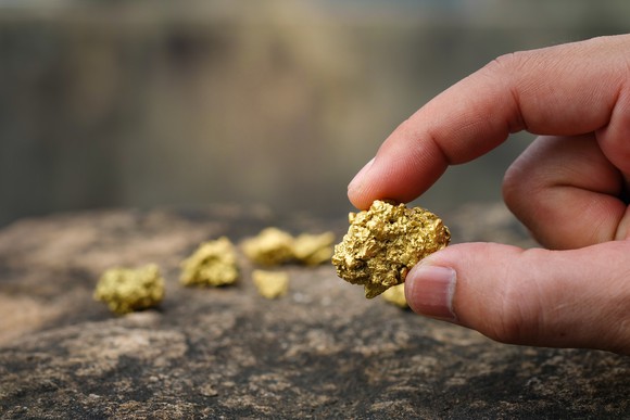 A person holding a piece of gold ore between thumb and finger.